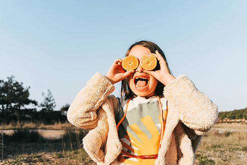 Une enfant joue avec des oranges en plein soleil.